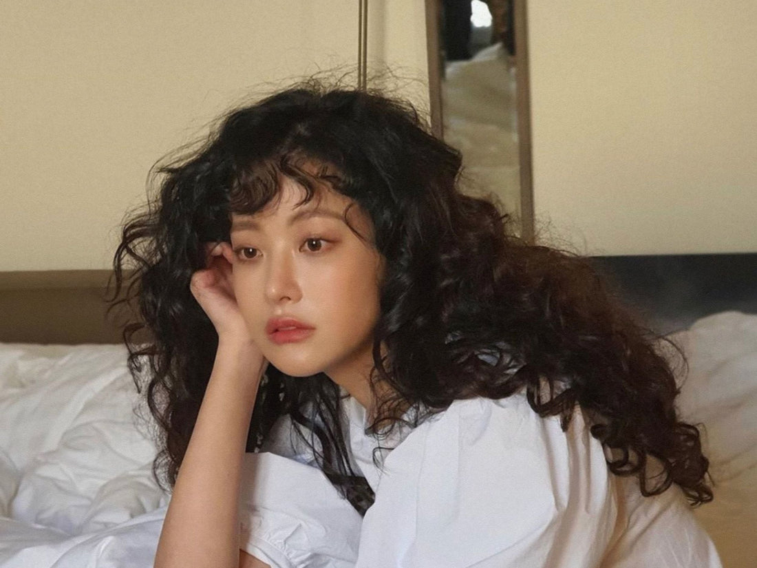 Photo of a girl with long, black, curly hair sitting on a bed