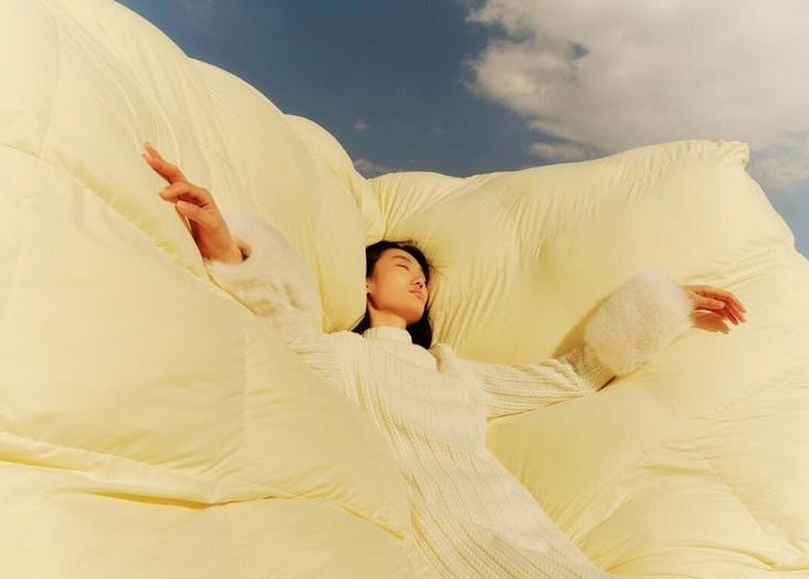 Image of a woman wearing a white dress laying down on a fluffy, white comforter