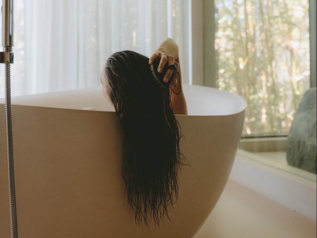 Photo of a woman in the bathtub brushing her long hair using the scalp brush