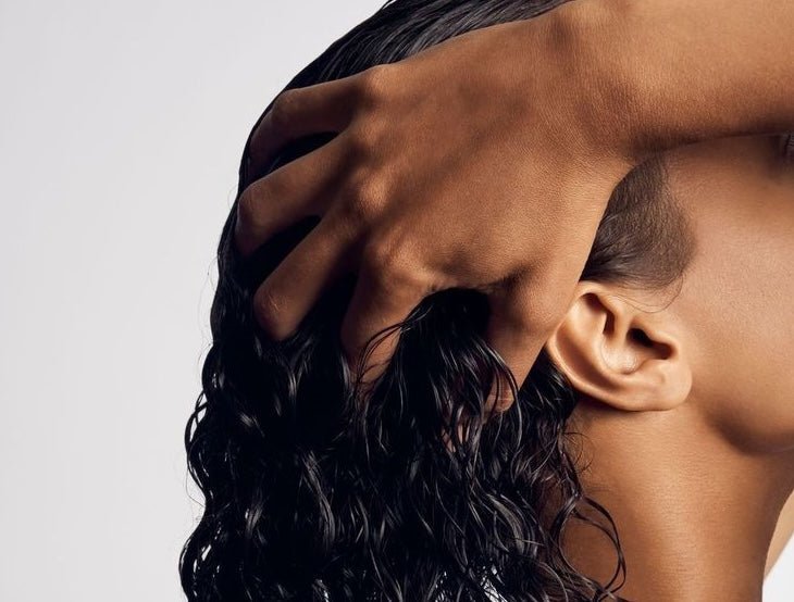 Photo of a woman with long, black, curly hair massaging her scalp